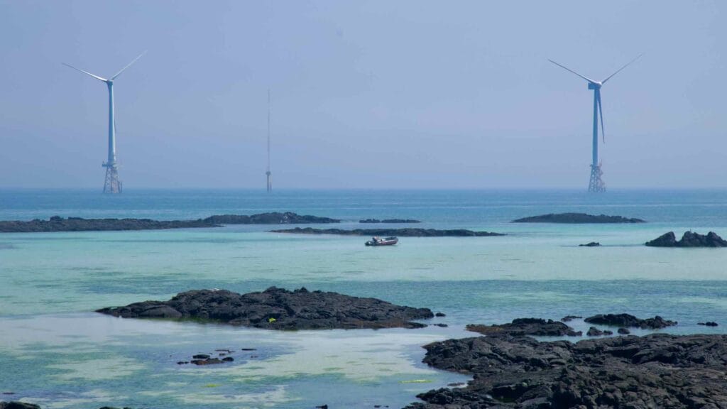 A small boat crosses emerald shallows below offshore turbines.
