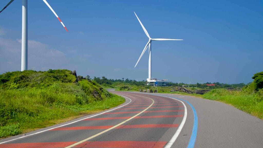 Curving coastal road and bike lane pass beneath towering wind turbines near Gimnyeong.