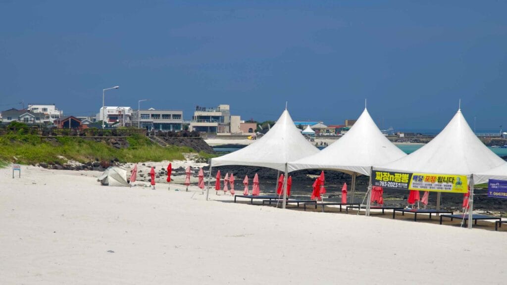 Shade canopies and red umbrellas line the white sands at Gimnyeong Seongsegi Beach.