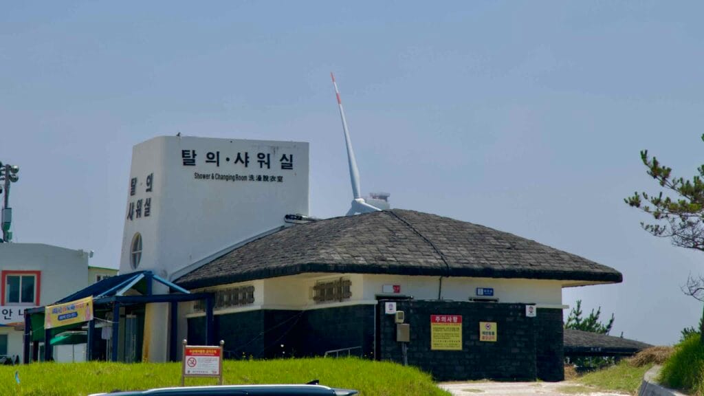 Shower and changing room building overlooks the beach as a turbine blade peeks above.