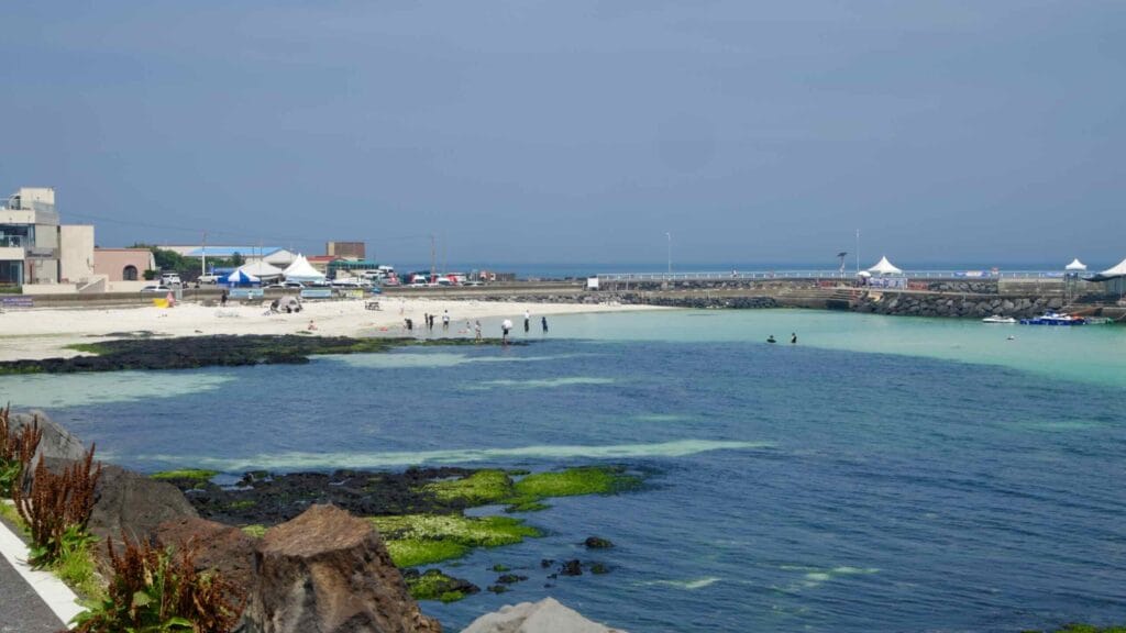 Families wade in the calm, shallow lagoon at Segial Beach between the breakwaters.