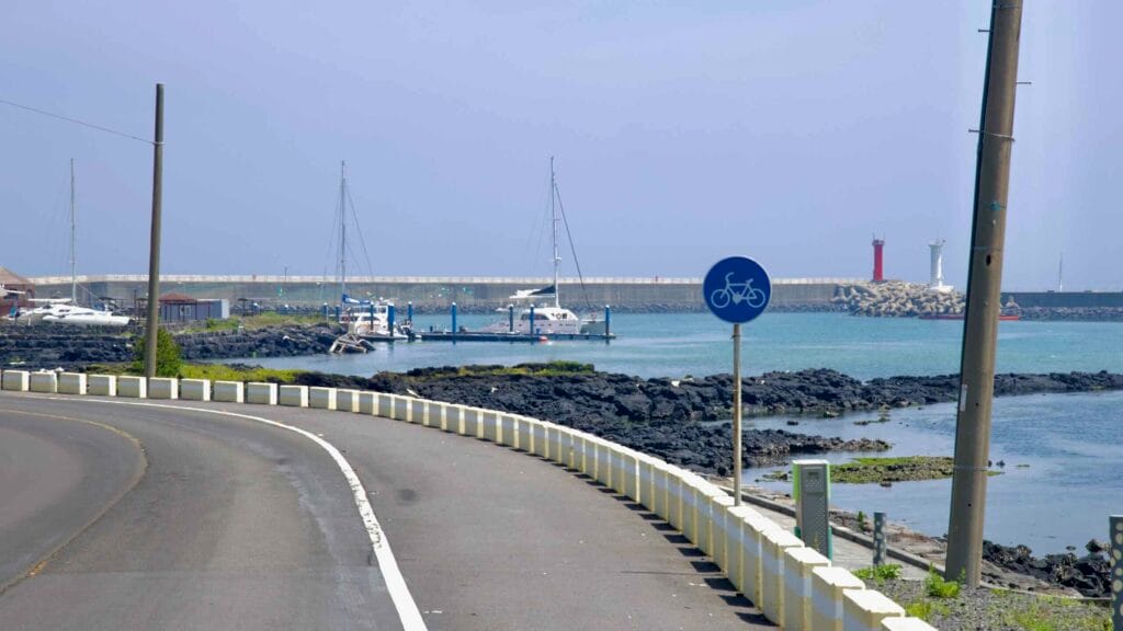 A blue bicycle sign marks the coastal road beside the marina at Gimnyeong.