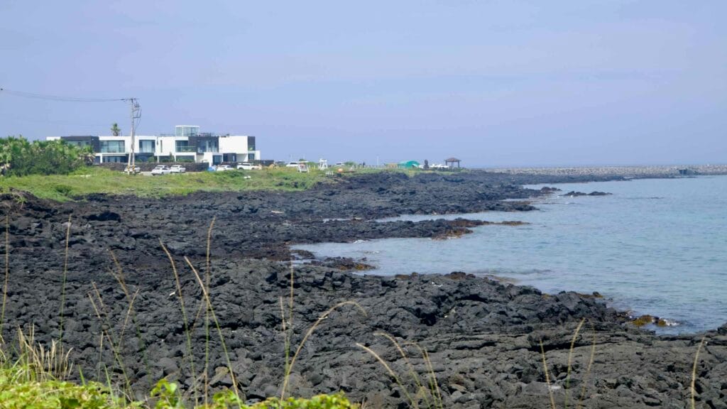 Basalt ledges front modern white villas along the curved lava shoreline at Dongbok.