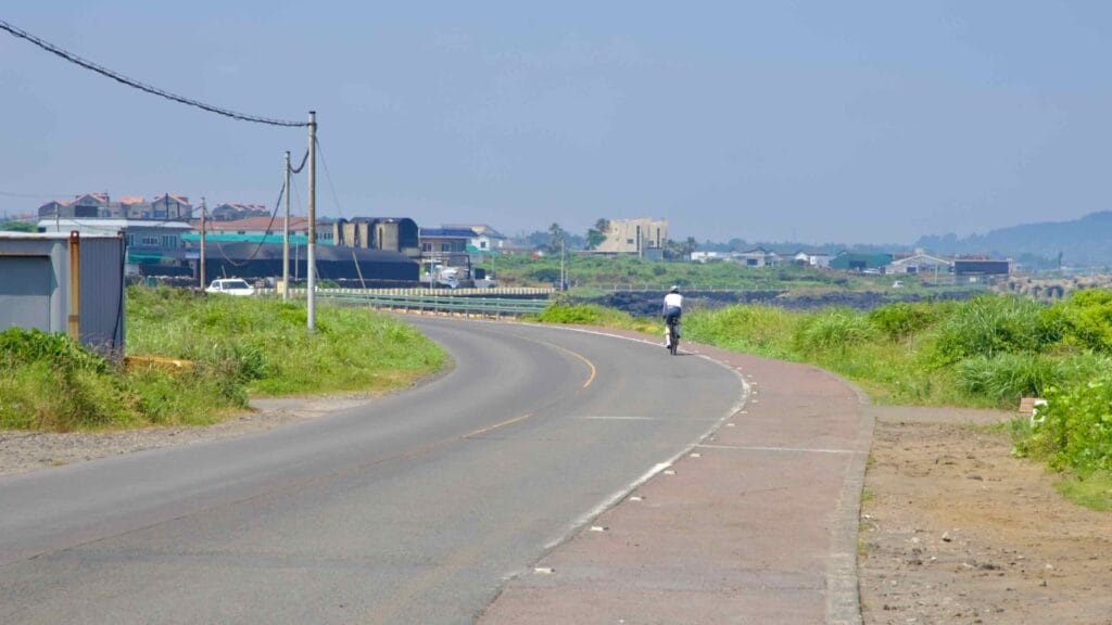 A solo cyclist rides the gently curving coastal road near Dongbok.