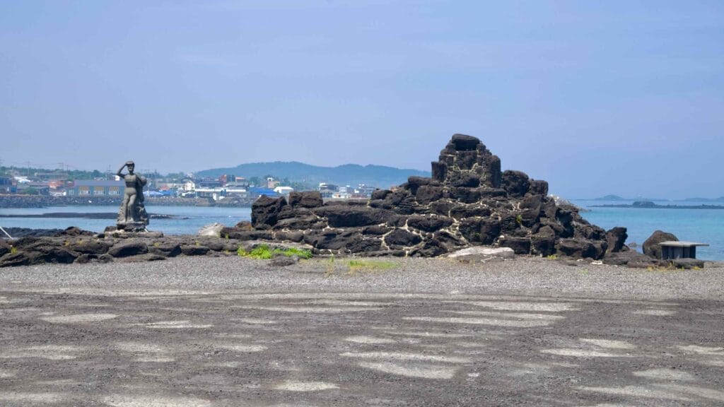 A haenyeo statue and a lava mound stand along Dongbok’s shoreline.