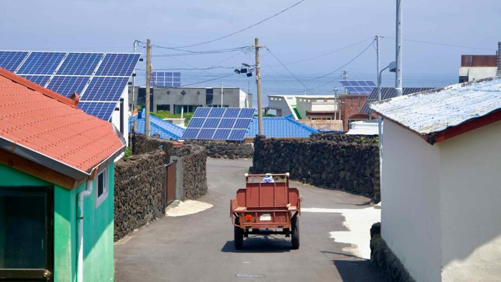 A village with lava-stone walls and solar rooftops descends toward the sea in Dongbok-ri.