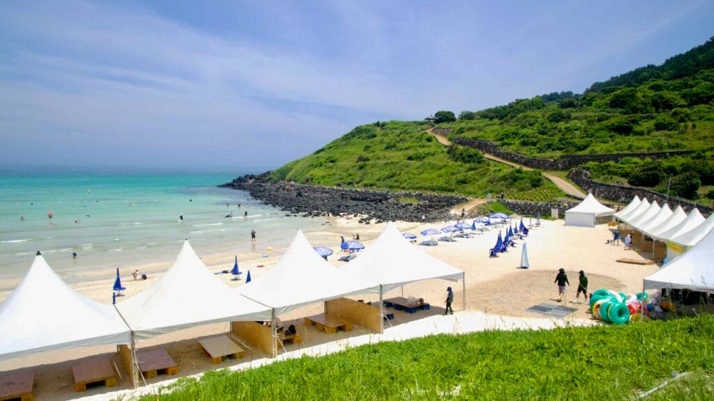 Turquoise water and white sand fill Hamdeok Seoubong Beach below Seoubong’s hill.