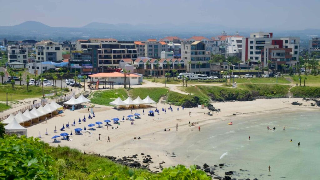 From Seoubong’s ridge, tents and umbrellas line Hamdeok Beach with city blocks beyond.