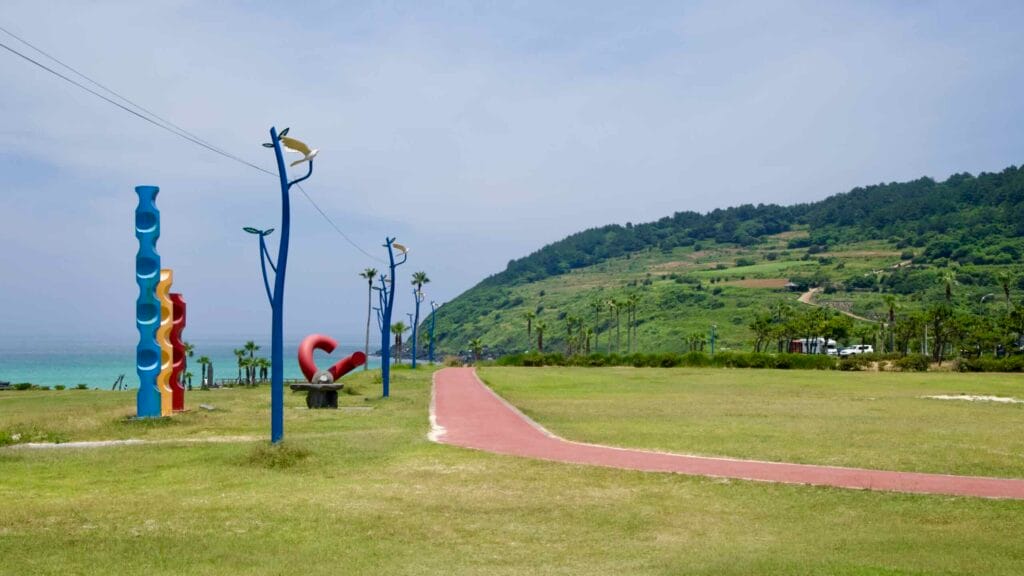 A red walking path winds past seaside sculptures and whimsical lampposts at Hamdeok.