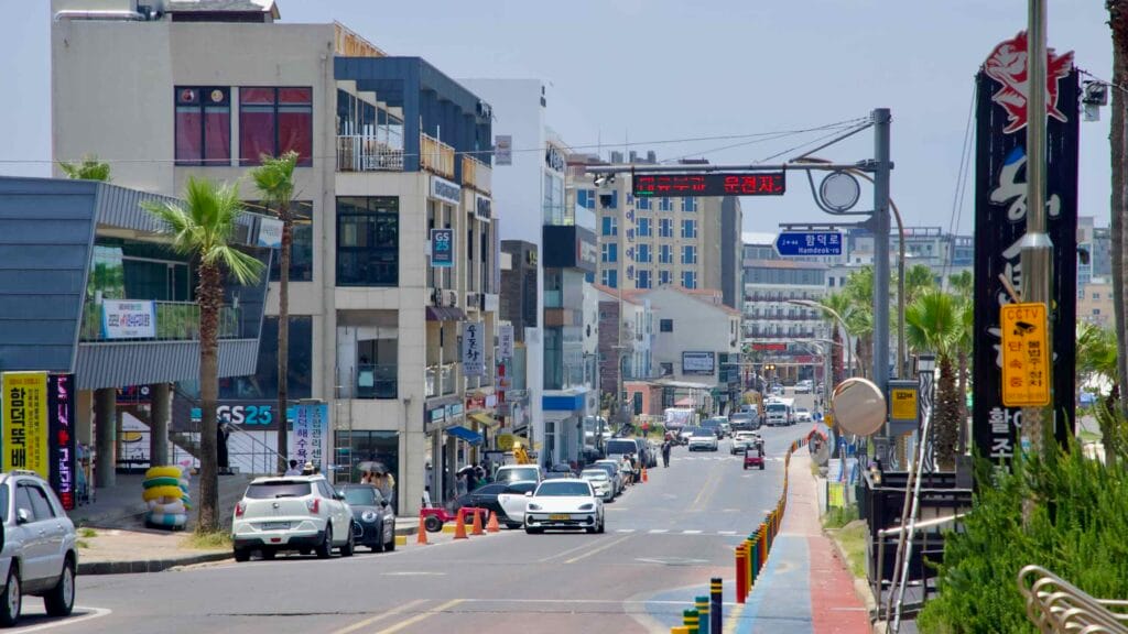 Traffic and pedestrians move along Hamdeok-ro lined with cafés, shops, and palm trees.