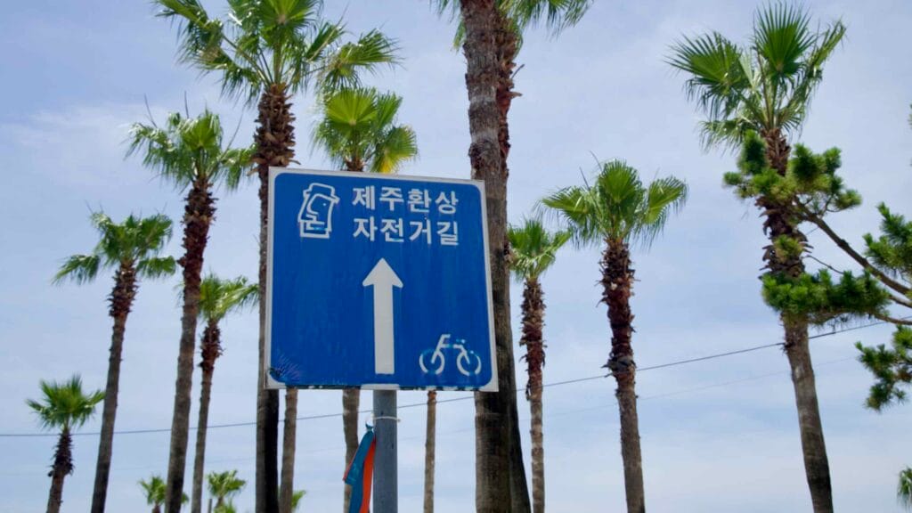 A blue Jeju Fantasy Bike Path sign points ahead near Hamdeok Seoubong Beach.