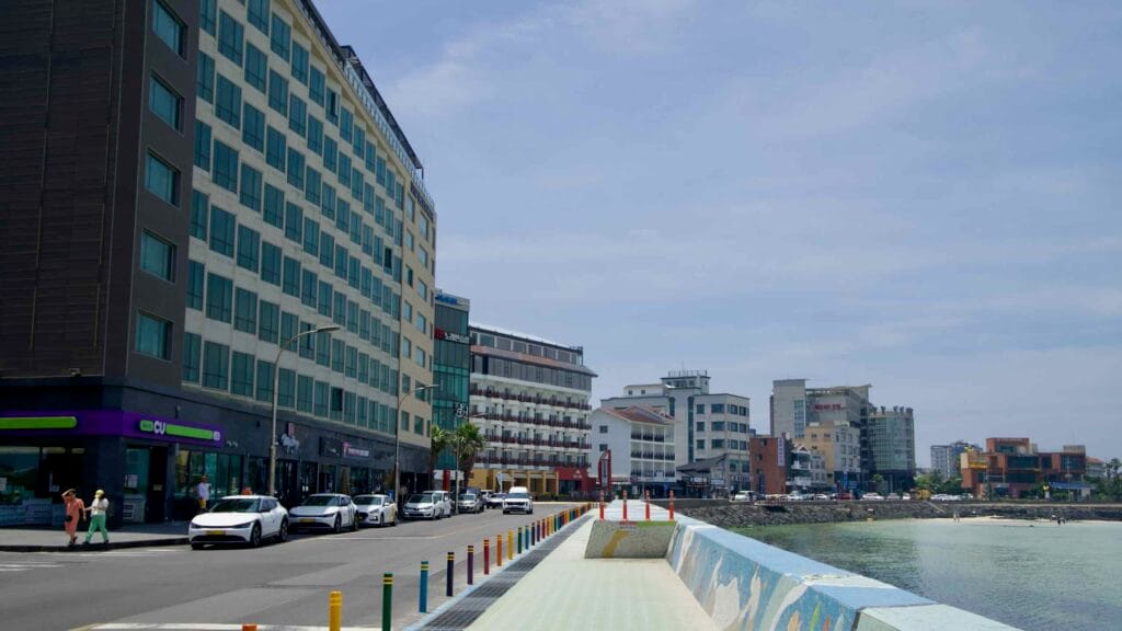 A tiled seawall promenade curves beside the water at Hamdeok as hotels and cafés.