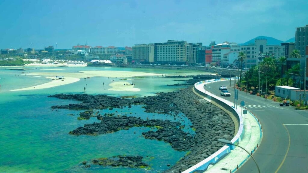 Coastal road curves past basalt reefs toward Hamdeok Seoubong Beach.