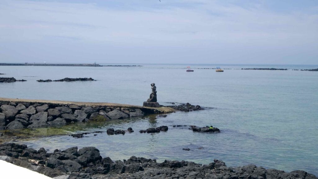 A stone sculpture of a haenyeo diver stands on a lava outcrop at Shinheung’s shore.