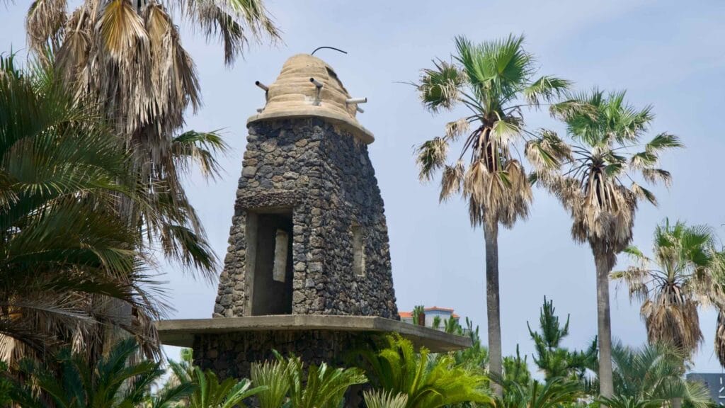 A conical stone tower with a concrete cap rises amid palms and cycads near Shinheung.