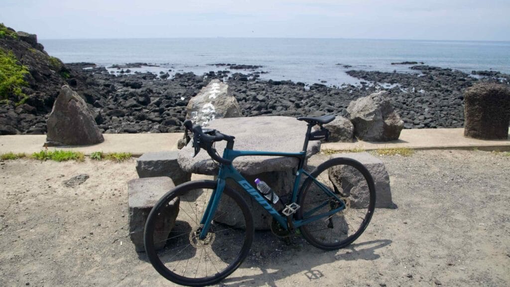Road bike on a basalt bench overlooking Shinheung’s rocky shore and calm, reef-lined sea.