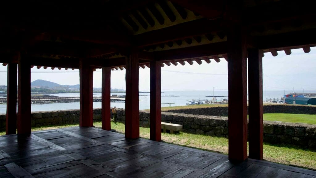 From Yeonbukjeong’s floor, pillars frame fish traps, breakwaters, and boats in Jocheon Port.