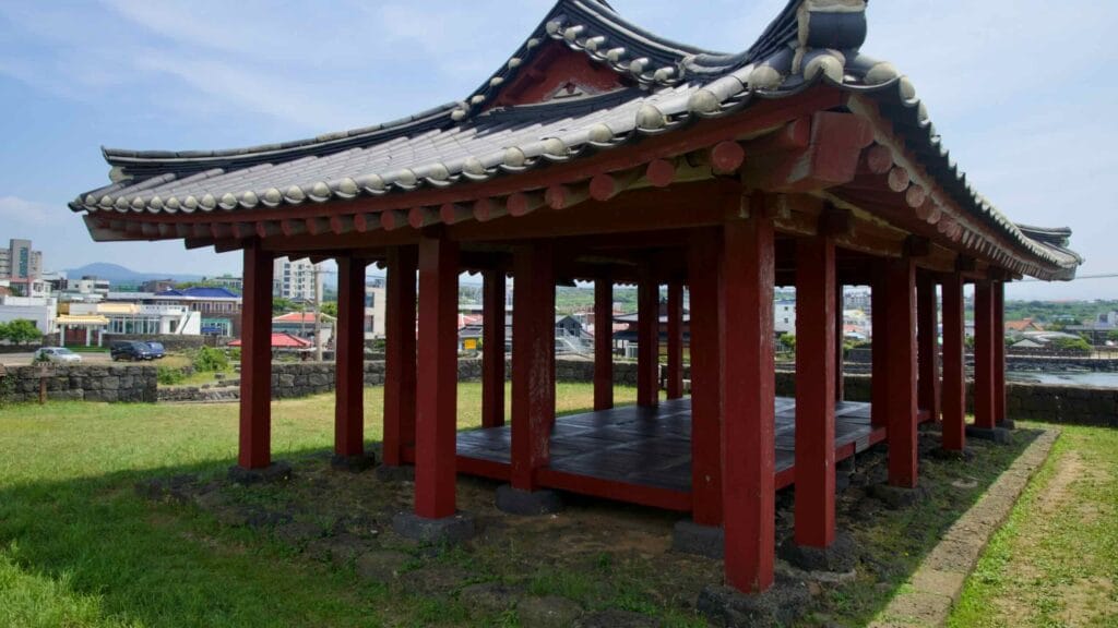 From Yeonbukjeong’s corner, red posts and tiled eaves frame rooftops and the coastline.