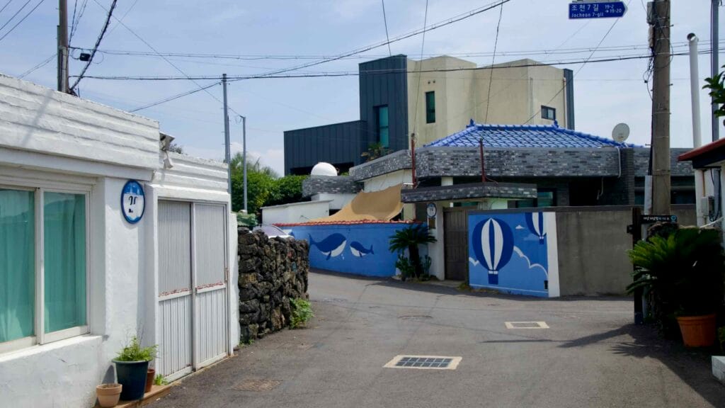 A quiet lane near Jocheon Port curves past low houses with blue tiles and murals of balloons.