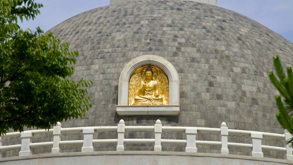 Gilded Buddha relief sits in a niche on the stupa’s domed wall above white railings.