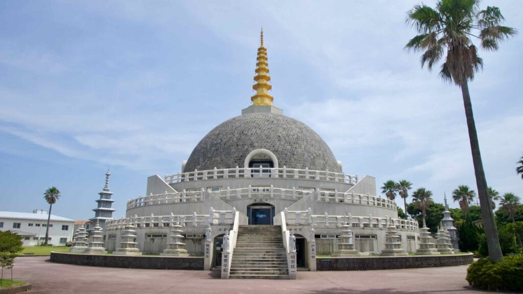 Frontal view of Buddha Sharira Stupa shows central stair, tiered railings, pagodas, and tall palms.