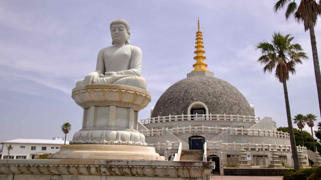 A seated Buddha faces the hemispherical stupa crowned by a golden spire.