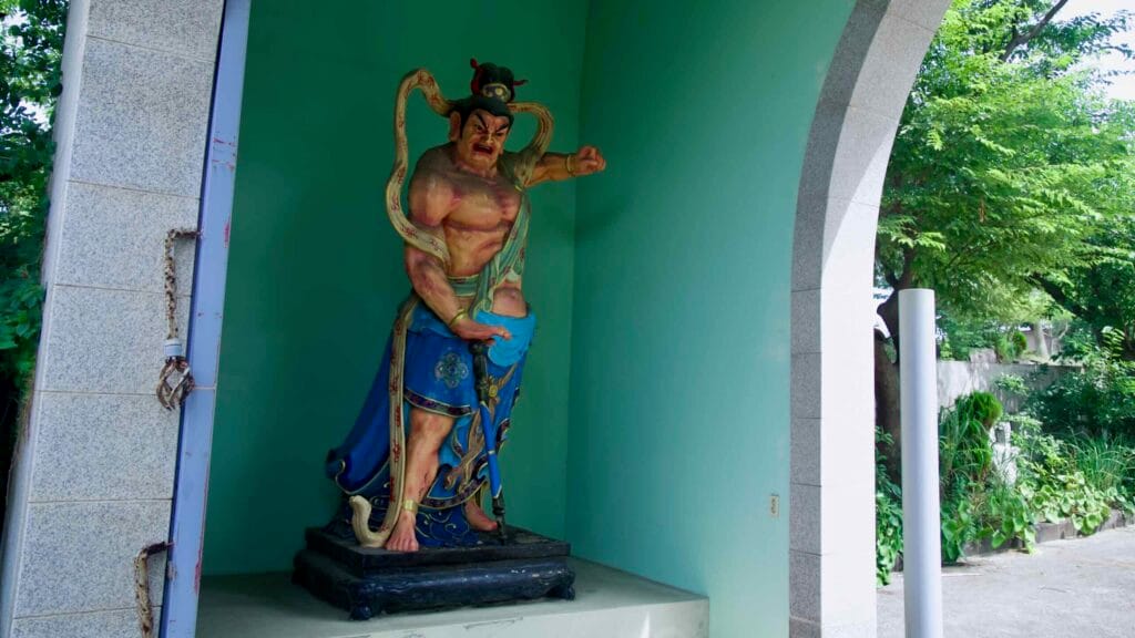 A guardian deity stands in a gate alcove, raising a fist and a sword.