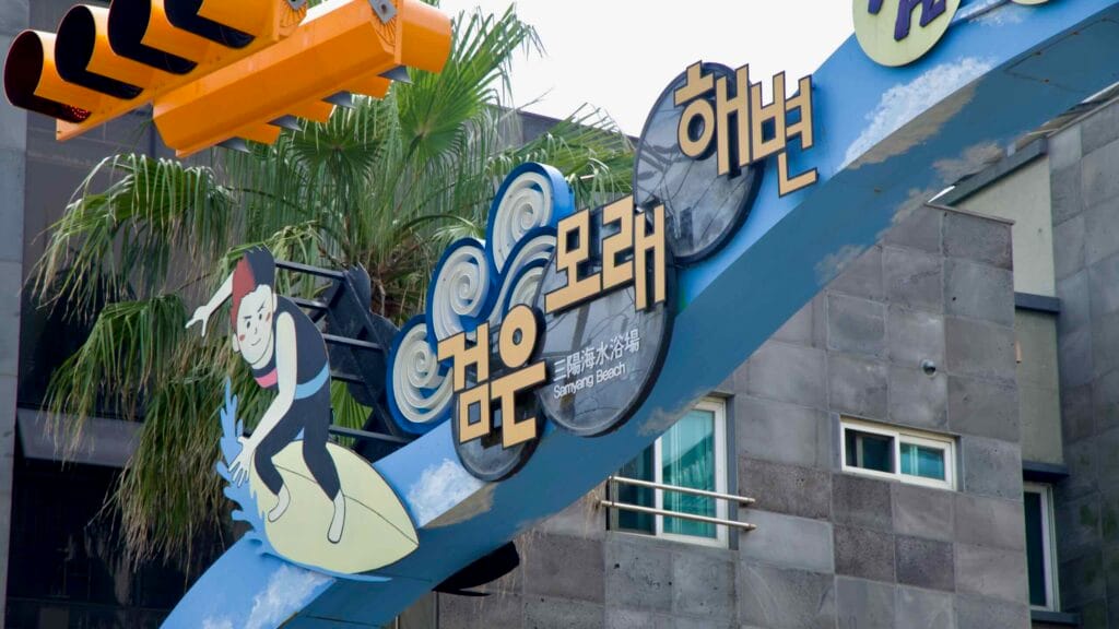 A surfer-themed gateway marks the entrance to Samyang Black Sand Beach.