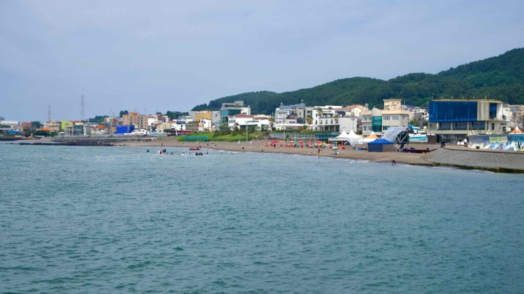Swimmers and umbrellas dot Samyang Black Sand Beach along the village waterfront.