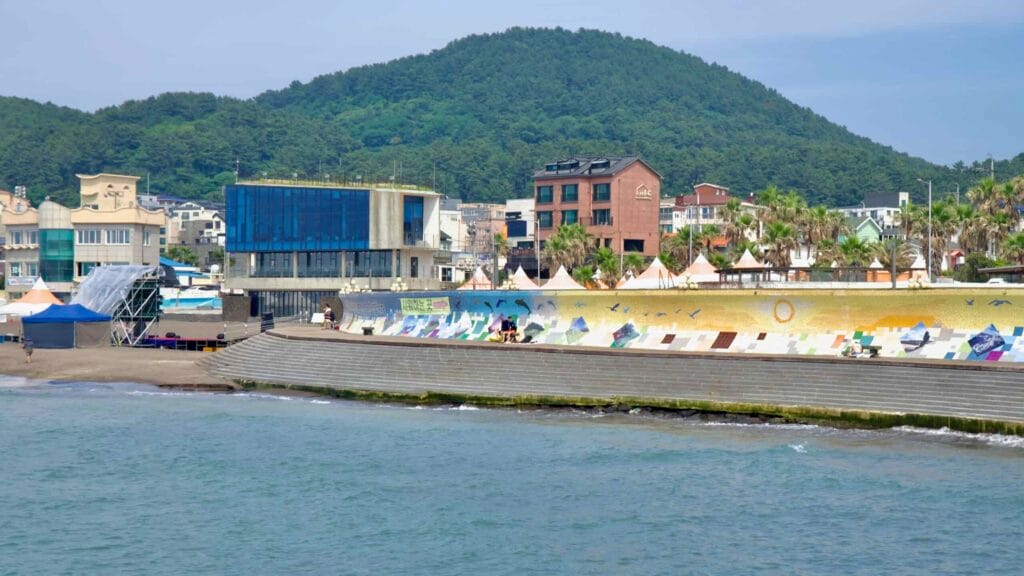 A colorful mosaic seawall lines the promenade below wooded hills.