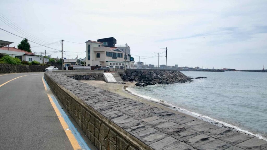 A narrow coastal road curves beside a basalt-block seawall at Samyang-dong.