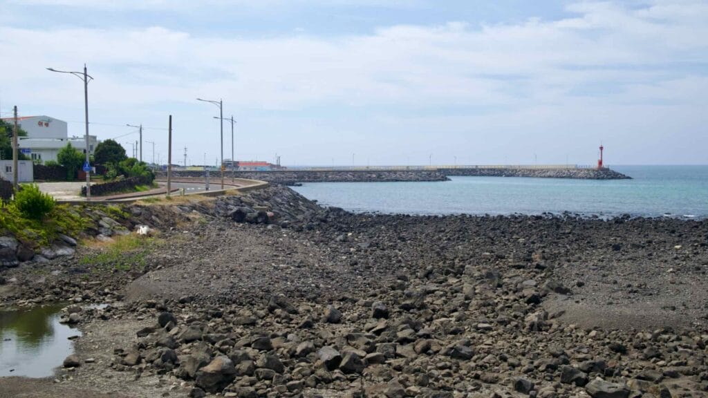 Basalt boulder fields frame an inlet leading to a long breakwater with a red beacon.