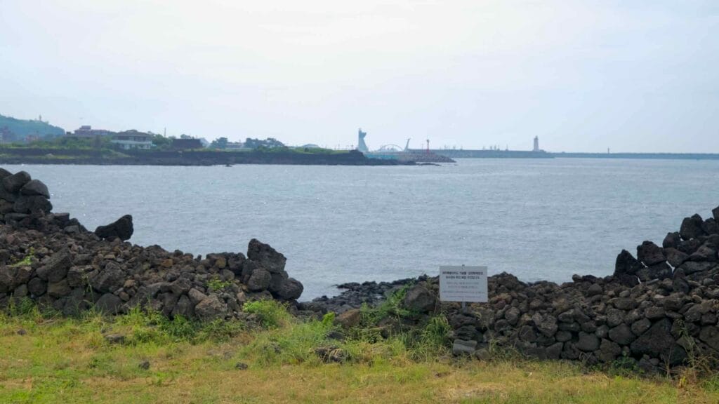 Low dry-stone walls frame the shore near Samyang as Byeoldobong and the Jeju Harbor.