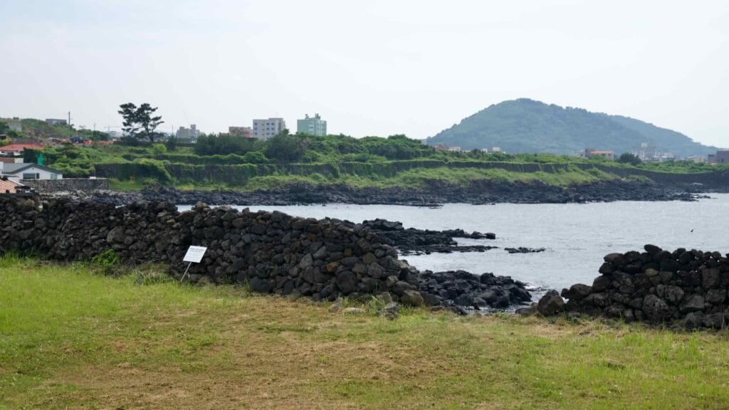 Basalt field walls and black rock ledges edge the Samyang coast, with Sarabong rising beyond.