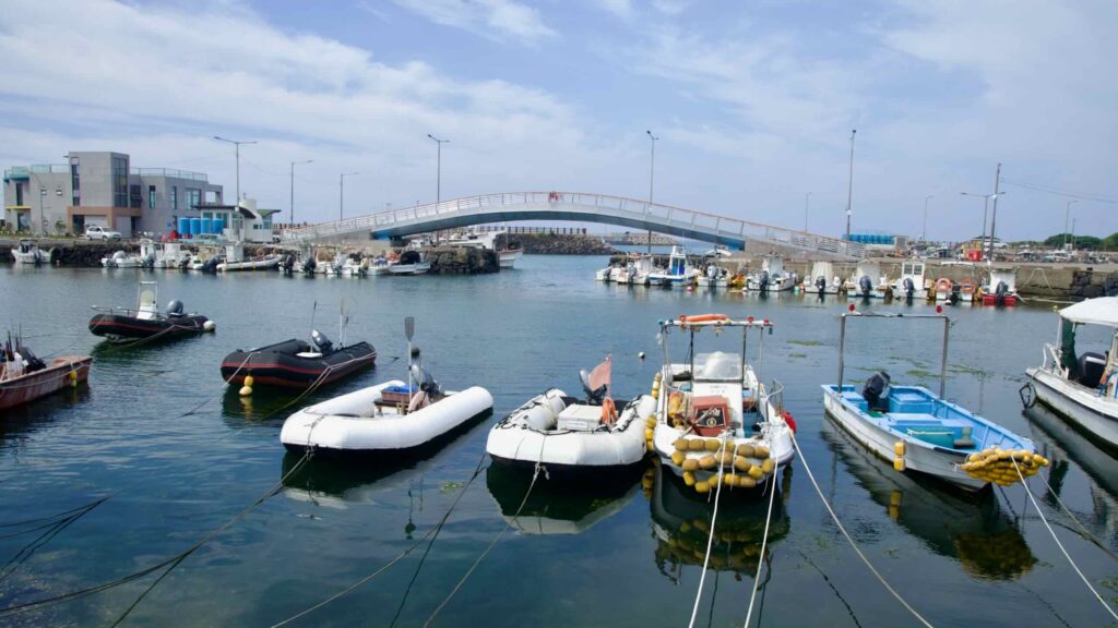 An arched pedestrian bridge crosses the harbor channel at Hwabuk as inflatable dinghies.