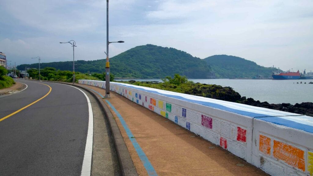 A curving coastal road and a footpath of color-stamped blocks trace Hwabuk’s shore.