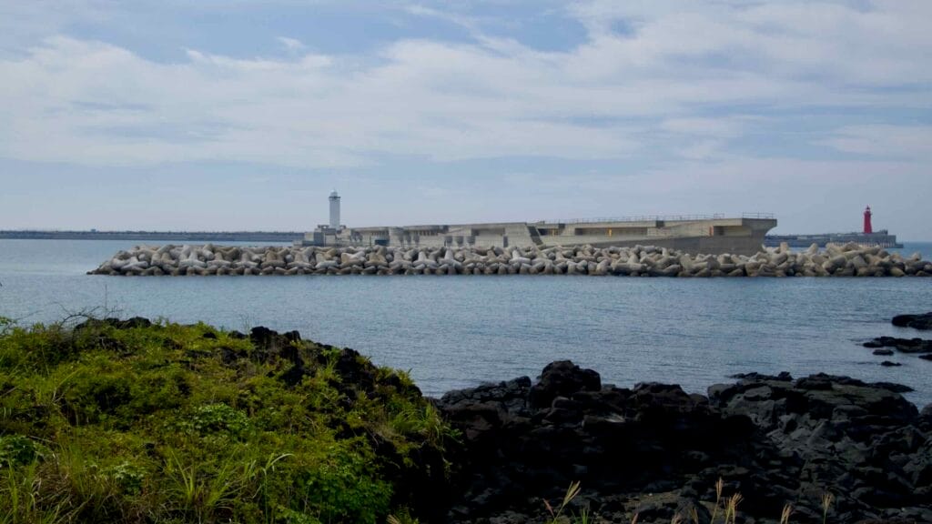 White and red lighthouses stand on opposing breakwaters at Jeju Harbor’s entrance.