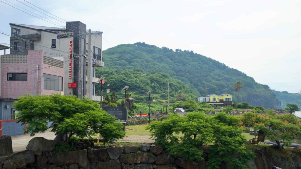 Cafes and guesthouses stand at the base of a green hillside along Hwabuk’s shore.