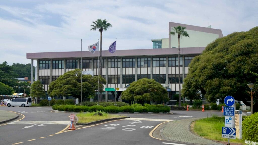 The main building at Jeju National University’s Sara Campus stands behind trimmed trees.