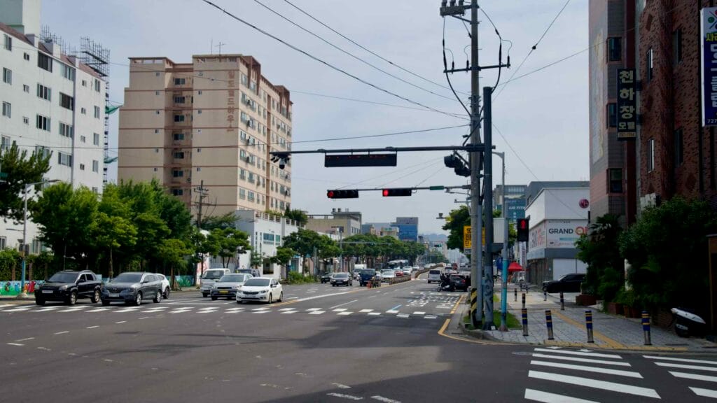 Traffic waits at a red light on a main Hwabuk road lined with mid-rise apartments.