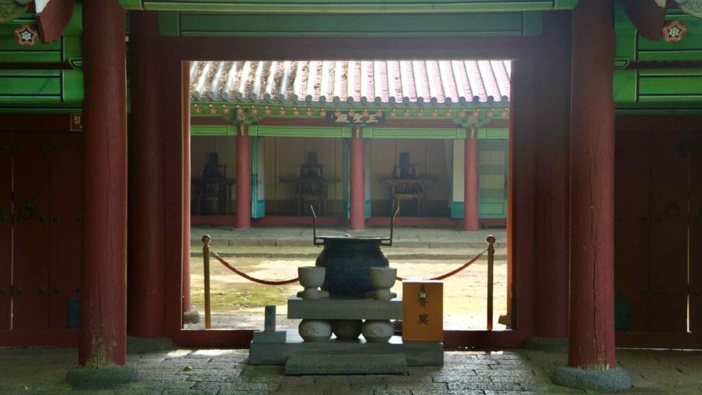 An incense burner and stone offering bowls sit before the inner gate, framed by red pillars.