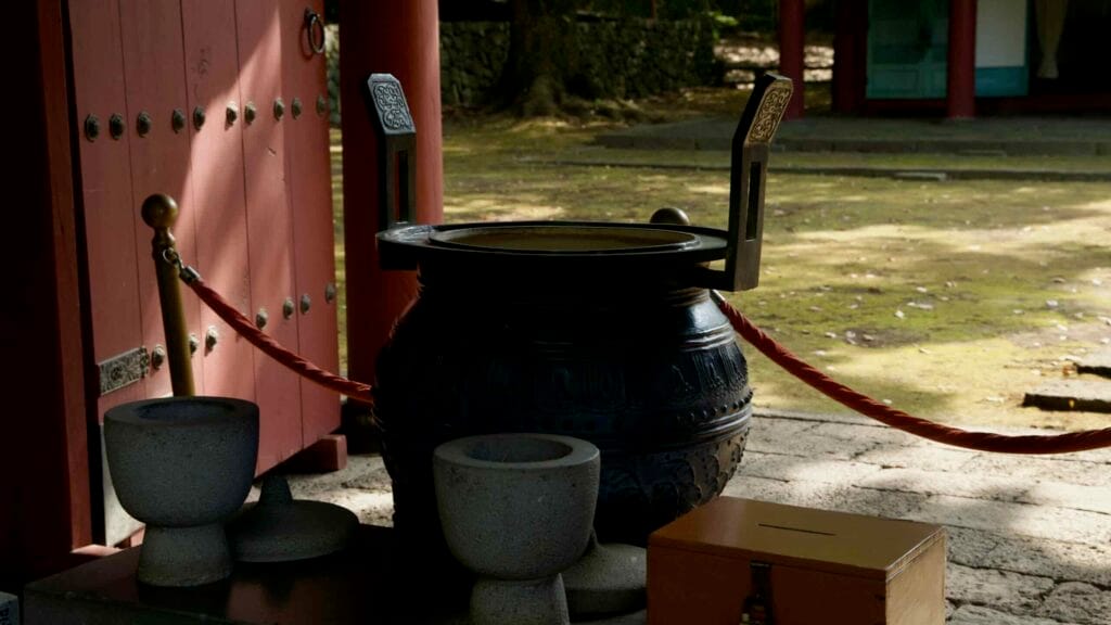 A close view shows the engraved ritual cauldron and offering bowls inside the gate.