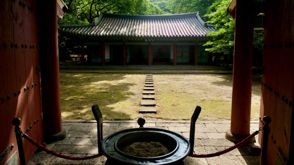 From the gate, stepping stones cross the mossy yard toward the opposite hall.