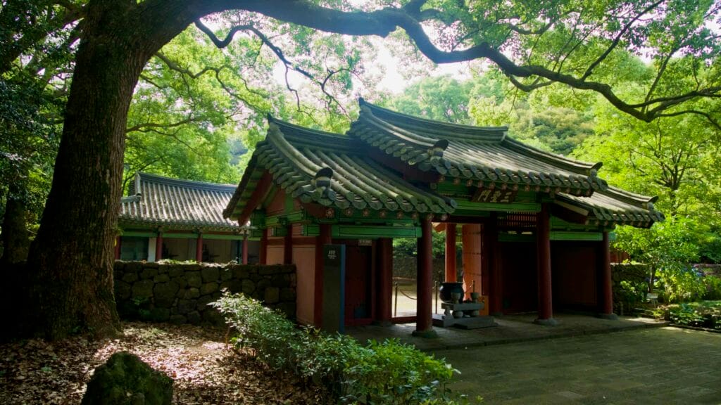 Twin gate pavilions sit beneath spreading branches, with stone walls and shaded paths.