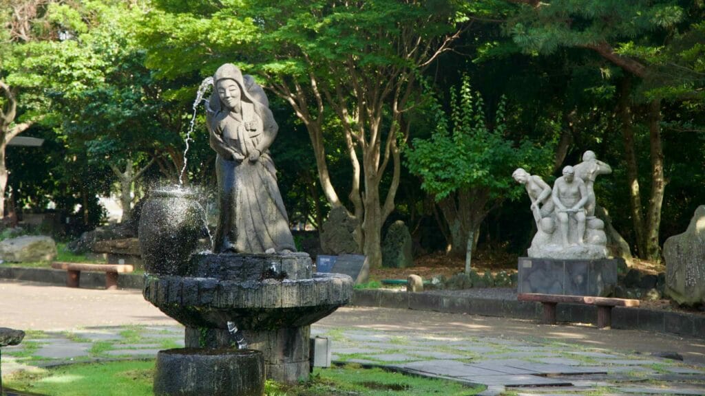 A stone fountain of a woman pouring water splashes beside the museum plaza.