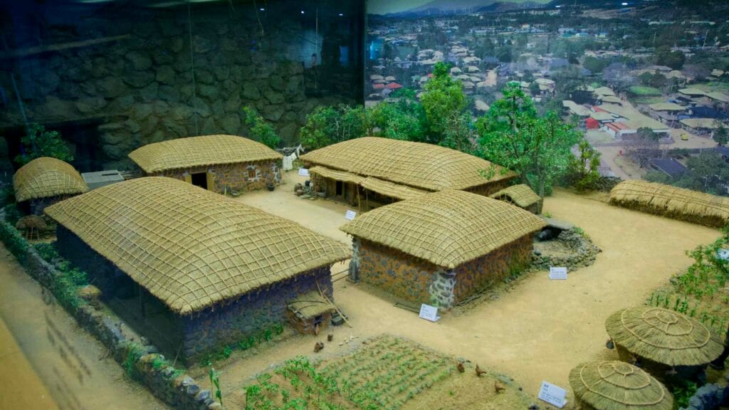 A diorama shows stone-and-thatch houses, garden plots, recreating a traditional Jeju village.