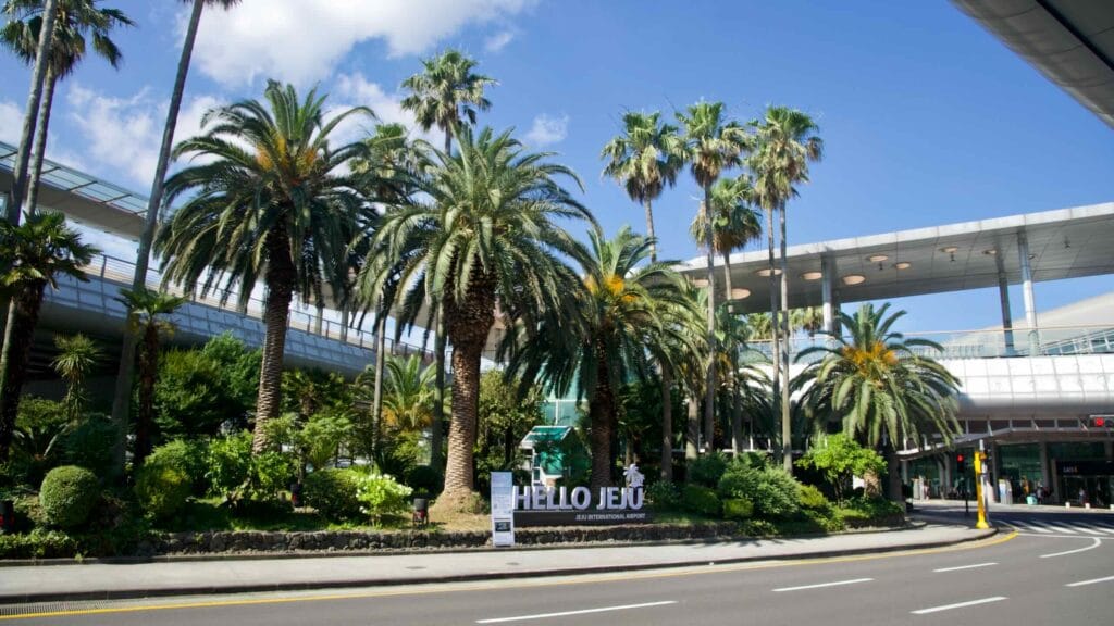 Palm trees and landscaping frame the 'HELLO JEJU' sign outside the airport.