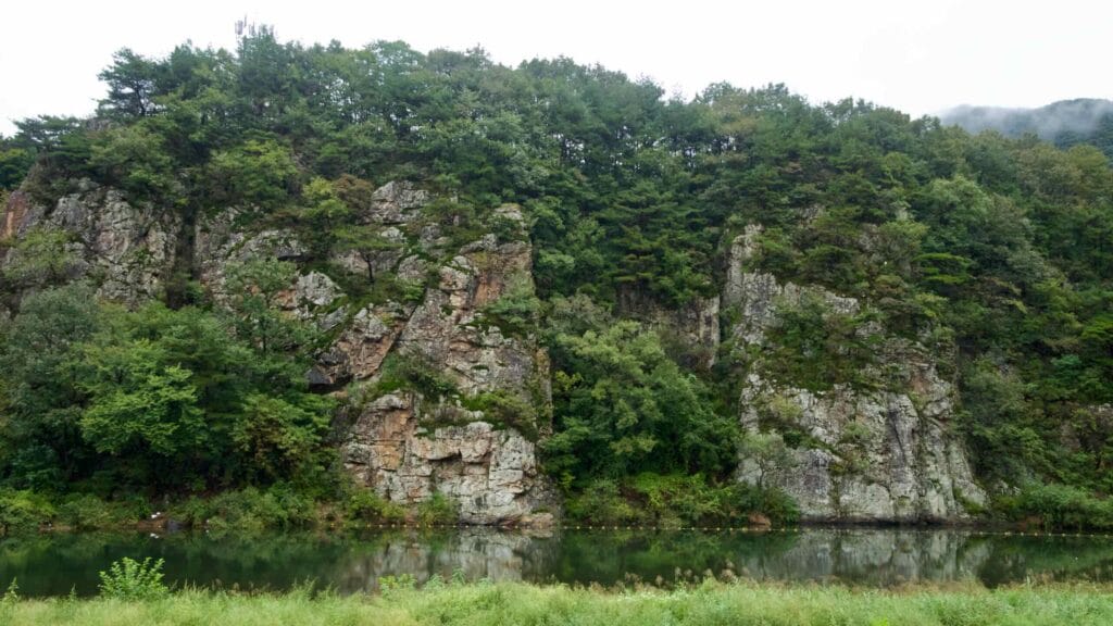 Pine-topped cliffs reflect in a calm river after rain.