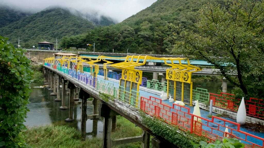 An elevated view shows the Omija Theme Tunnel bridge and colorful panels over the river.