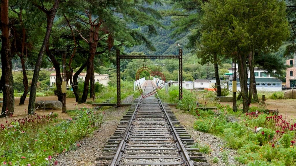 Another heart frame arches above disused tracks that reach a narrow bridge by village homes.